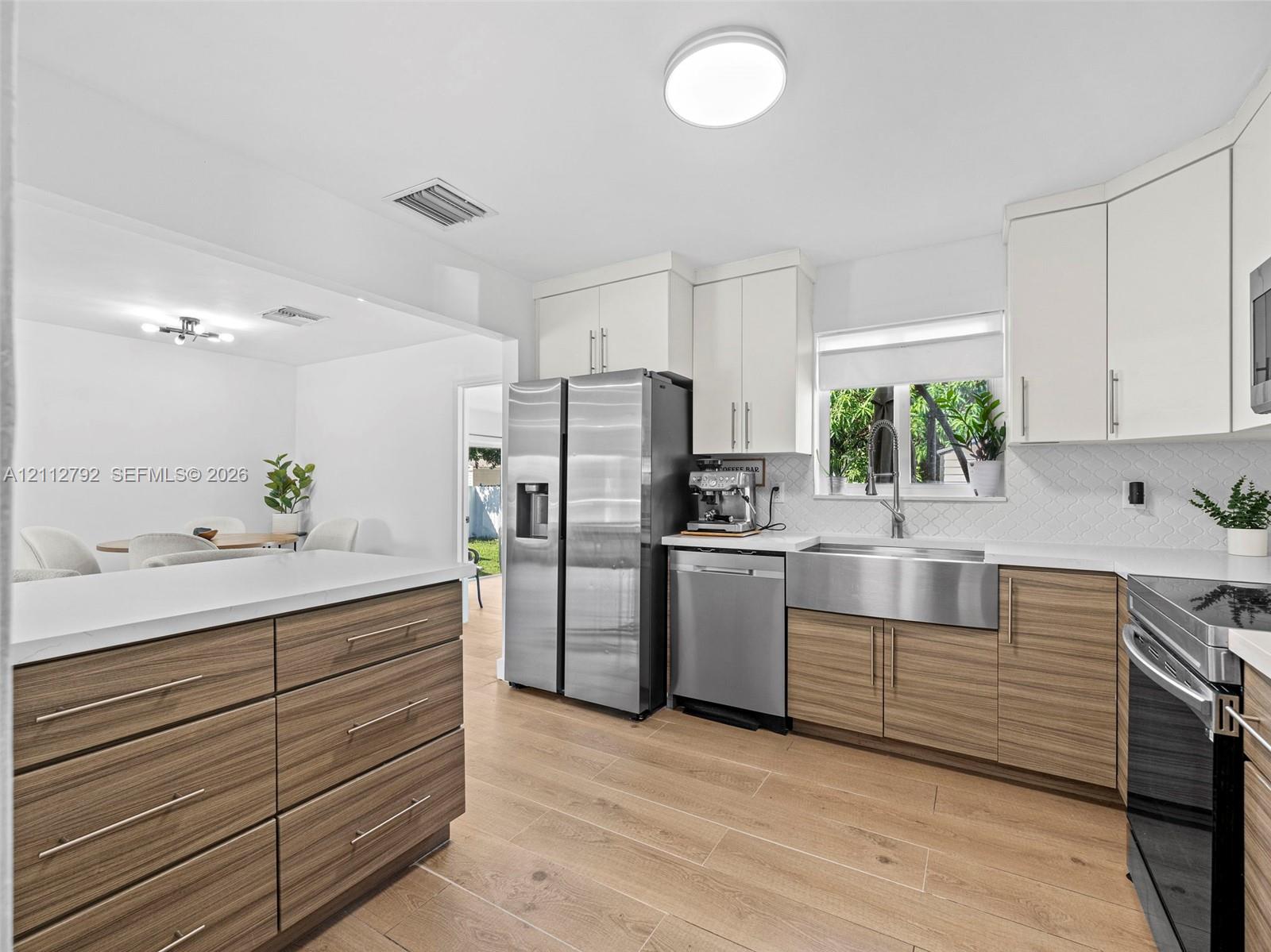 Kitchen featuring wood-finish cabinetry with flat-panel doors, quartz countertops, stainless steel farmhouse sink, wood-finish flooring, and stainless steel appliances