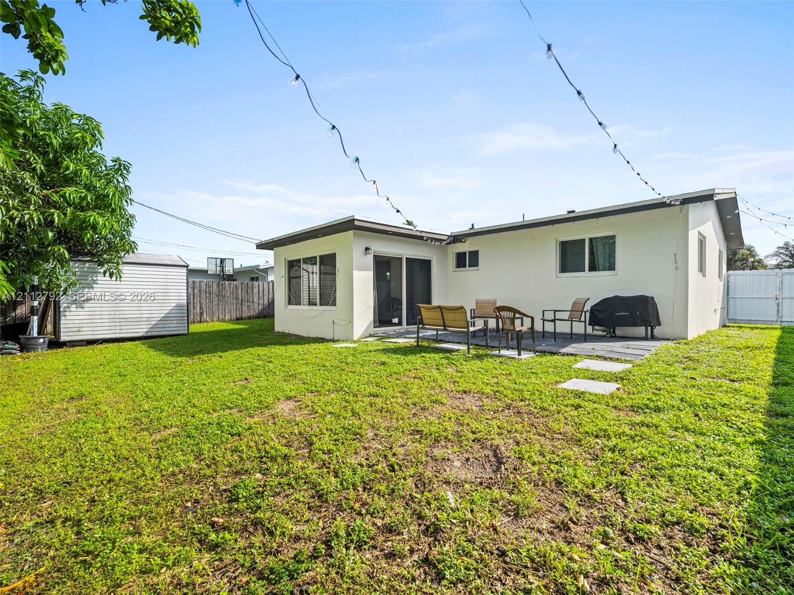 Rear exterior featuring a concrete patio, stucco siding, sliding glass doors, detached storage shed, and perimeter fencing