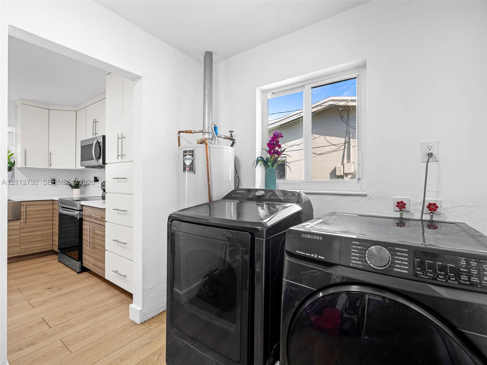 Utility room featuring wood-finish flooring, a vertical water heater, and a sliding window