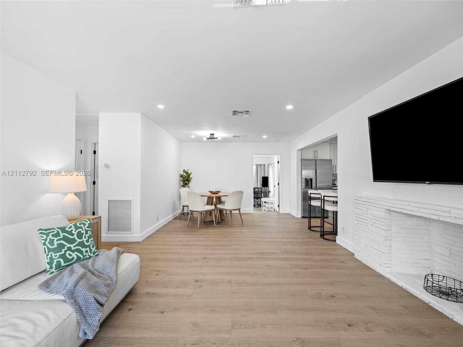 Open-concept interior featuring light wood-finish flooring, recessed lighting, and a painted brick fireplace surround