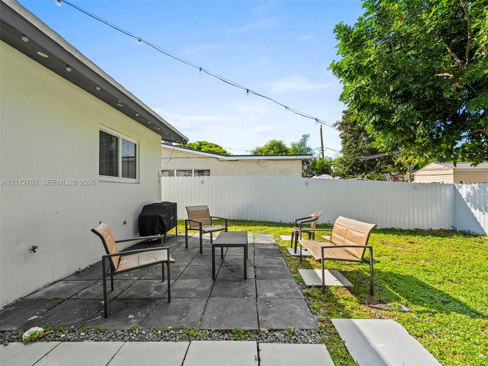 Rear patio featuring square stone pavers, enclosed by white privacy fencing and mature trees