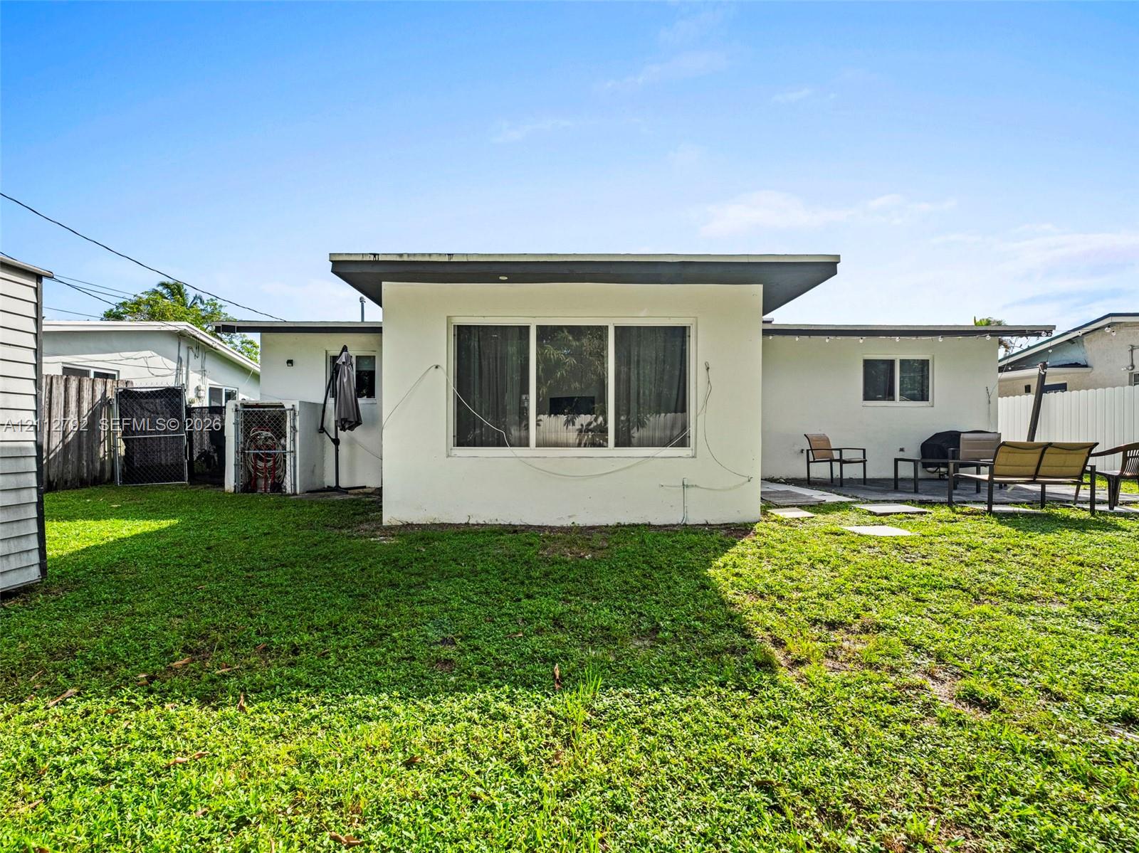 Rear exterior featuring a flat roofline, stucco siding, large picture windows, and a paved patio area set within a fenced yard