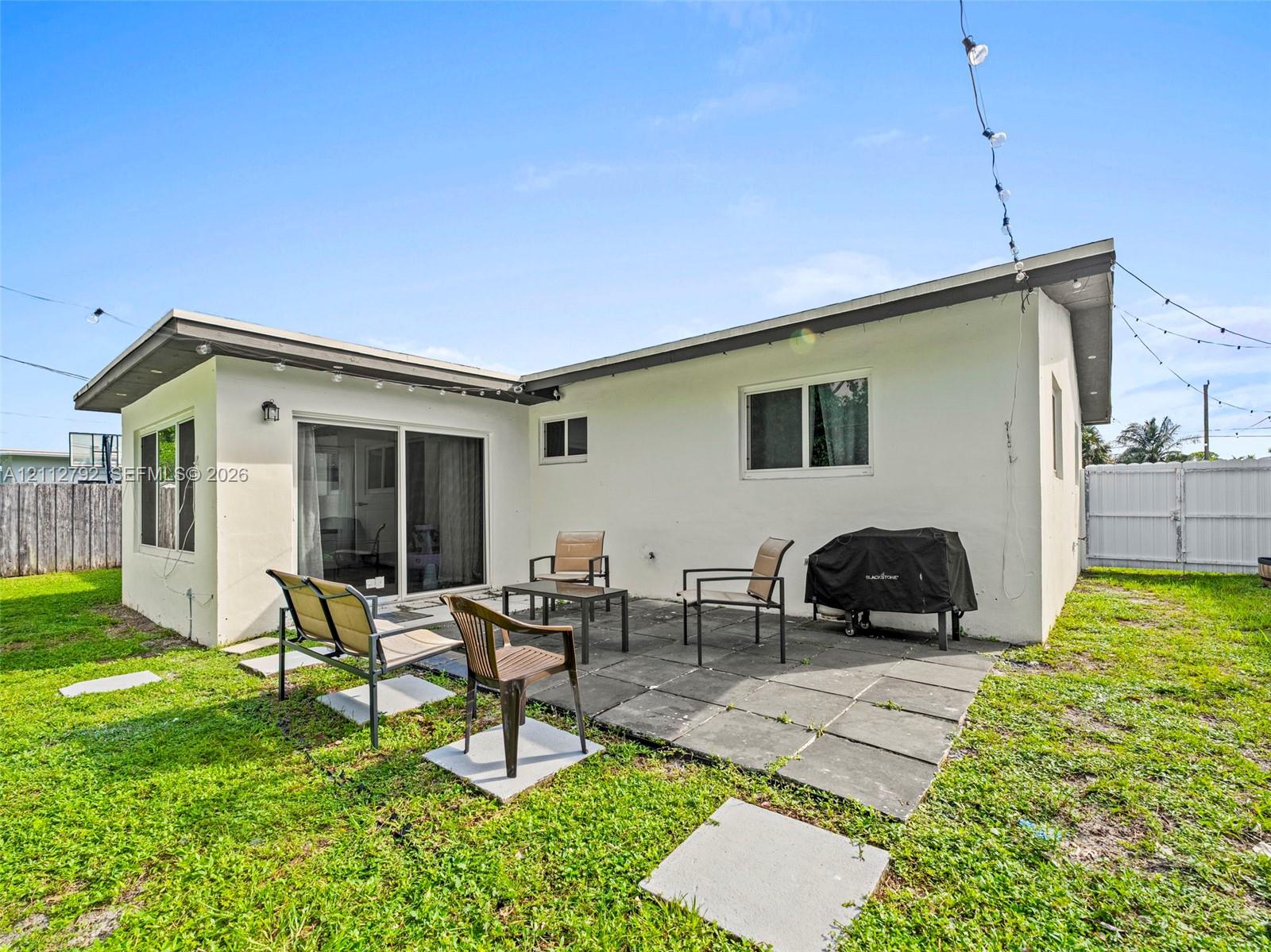 Rear exterior featuring a concrete paver patio, sliding glass door, white stucco siding, and a fenced backyard