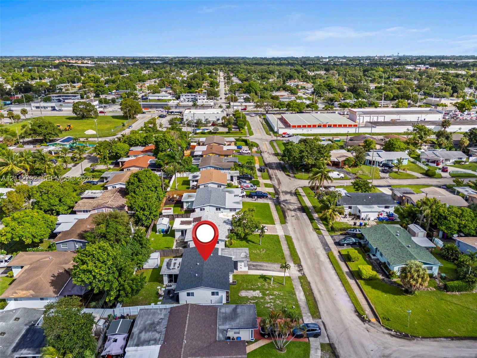 Aerial perspective featuring a single-story residence with a dark shingle roof, concrete driveway, and perimeter fencing on a landscaped lot