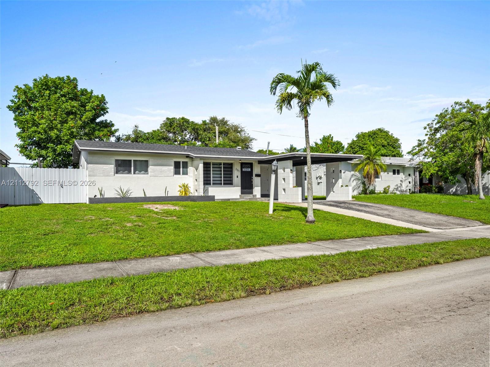 Single-story residence featuring a light-toned stucco exterior, asphalt shingle roof, attached carport, and a white privacy fence