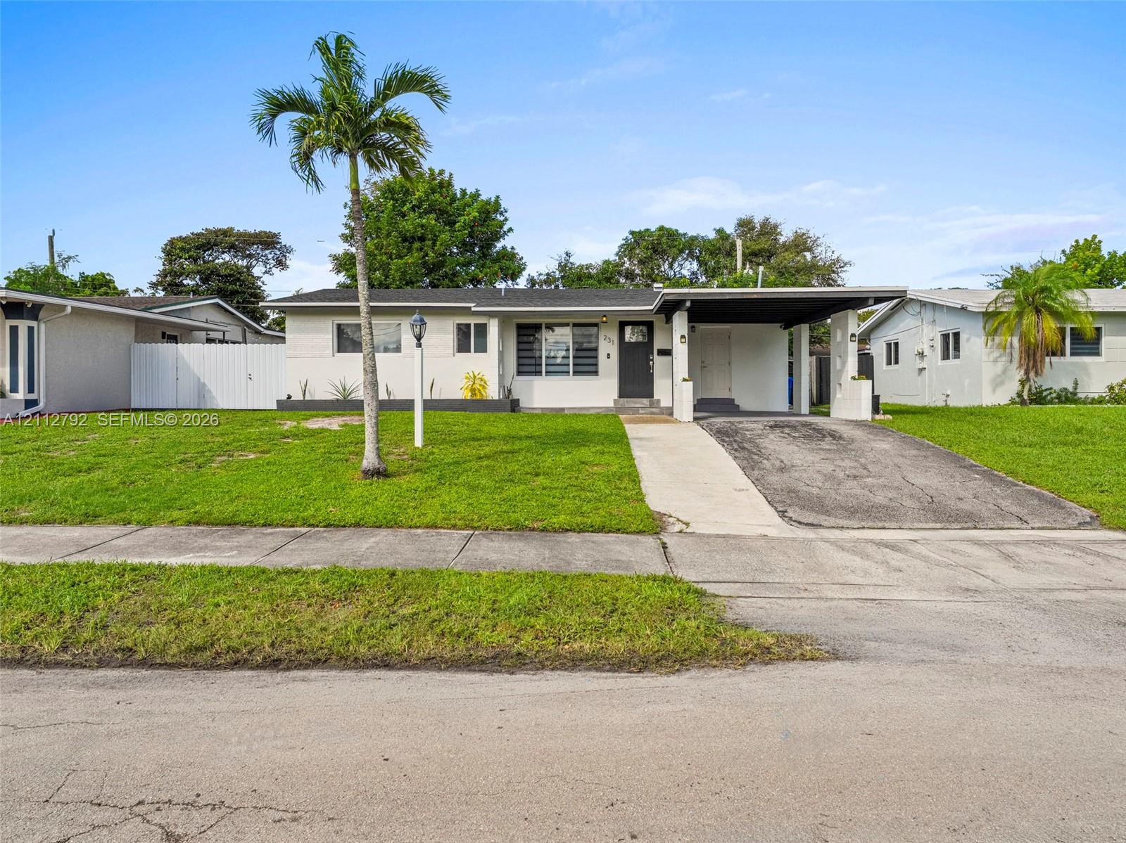 Single-story exterior featuring a concrete driveway, attached carport, manicured lawn, and exterior landscape lighting