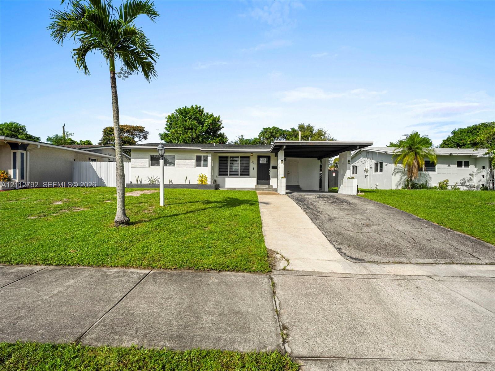 Single-story residence featuring a flat roofline, attached carport, concrete driveway, and exterior privacy fencing