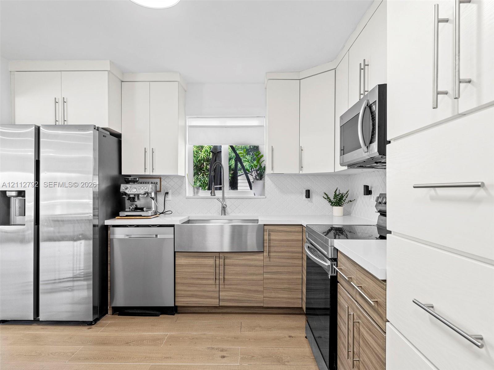 Kitchen featuring white upper cabinetry, wood-finish lower cabinetry, stainless steel apron-front sink, white countertops, and stainless steel appliances