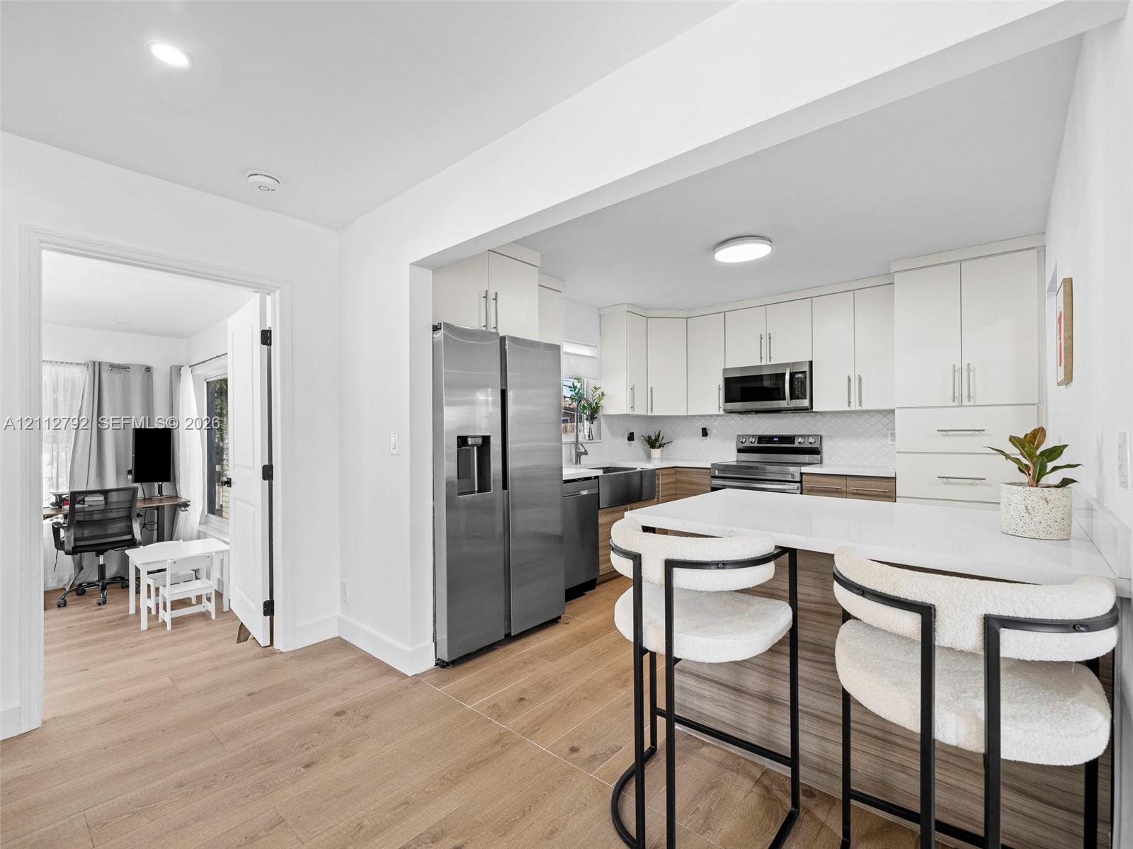 Kitchen featuring white cabinetry, wood-finish lower cabinets, stone-surfaced island, stainless steel appliances, and wood-finish flooring