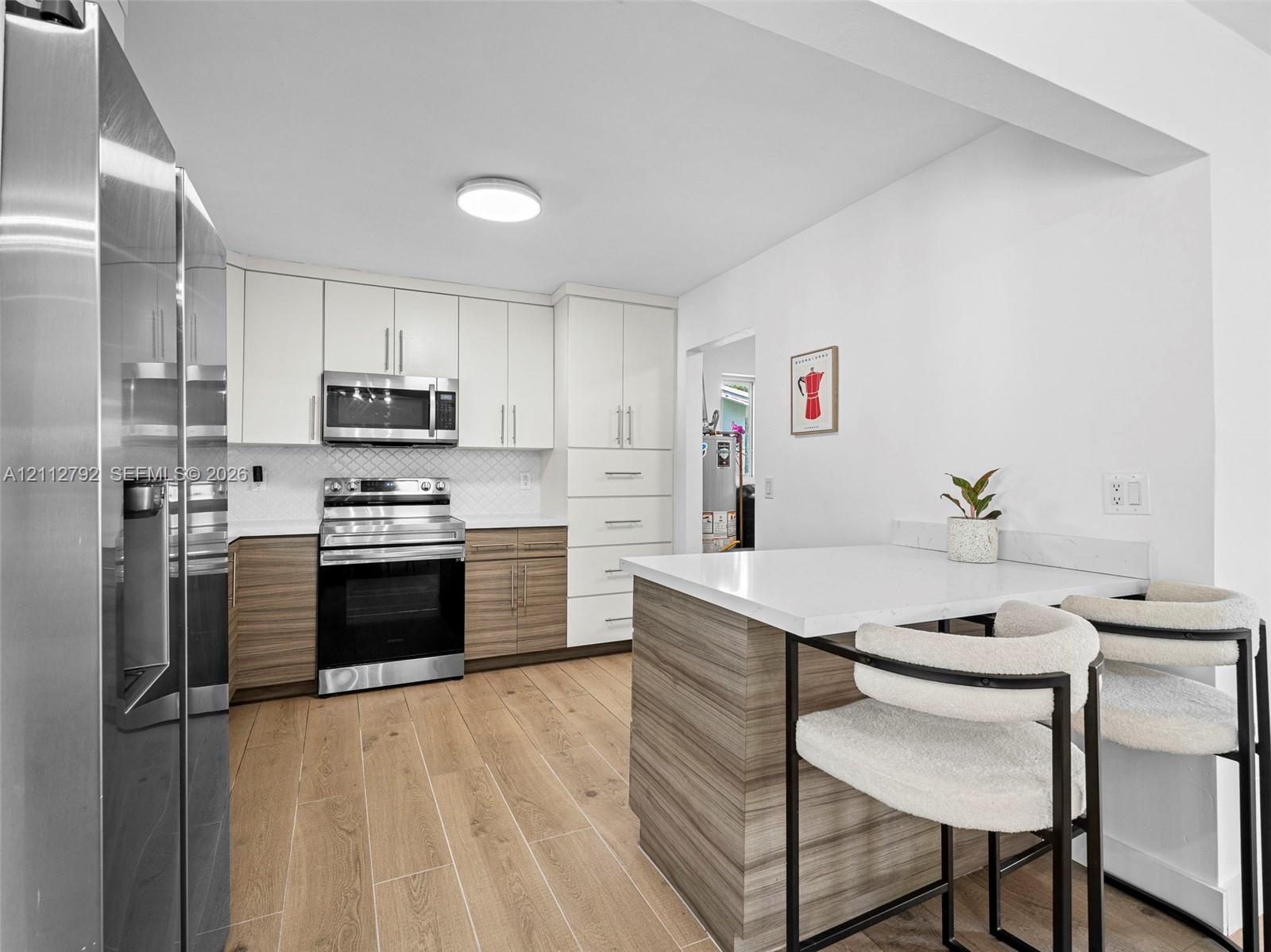 Kitchen featuring two-tone flat-panel cabinetry, stainless steel appliances, wood-finish flooring, and a built-in island with a solid-surface countertop