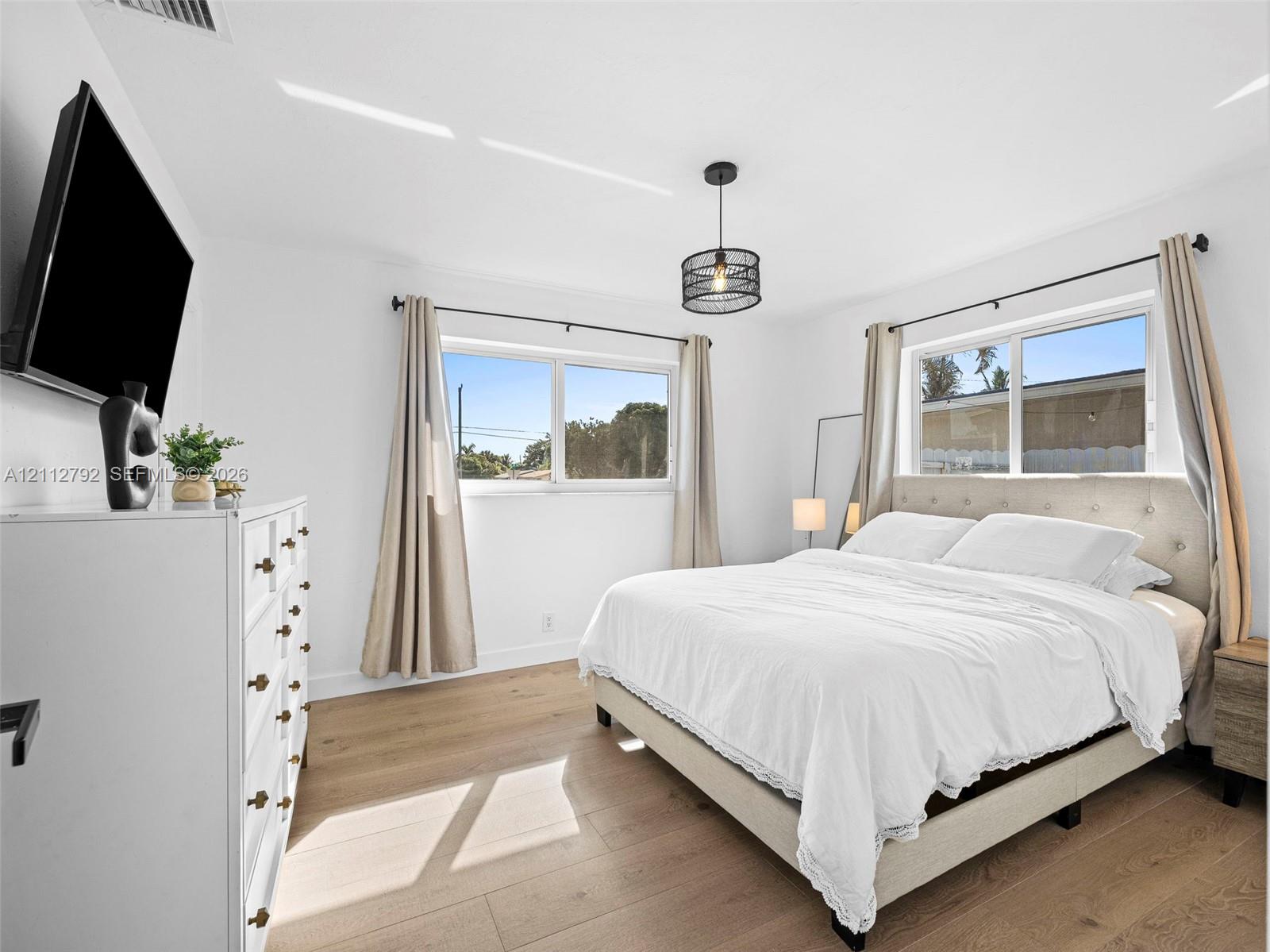 Room featuring wood-finish flooring, dual windows, and a cylindrical pendant light fixture