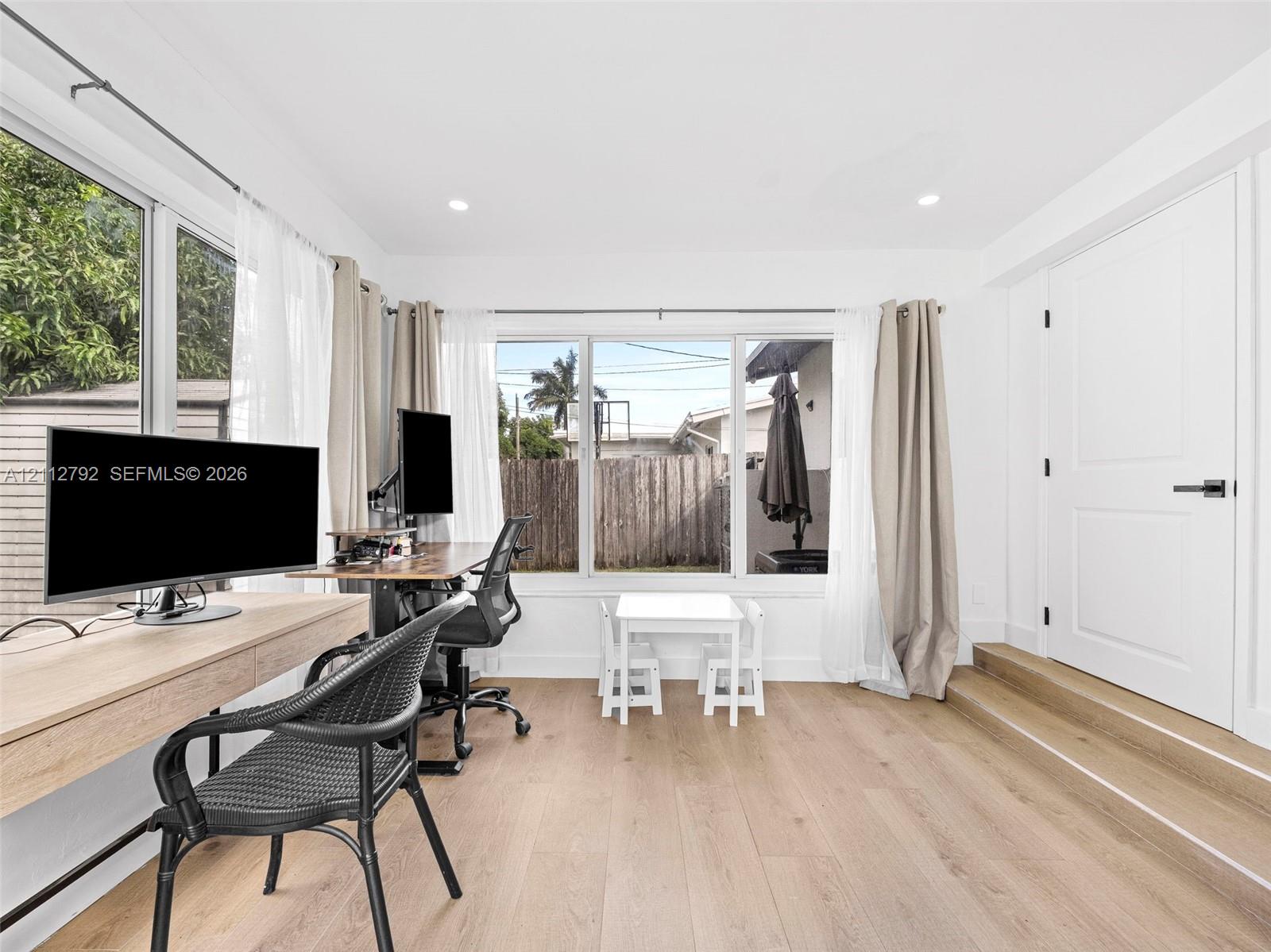 Room featuring wood-finish flooring, recessed lighting, expansive triple-pane window configuration, and a raised platform with a solid-core interior door equipped with matte black hardware