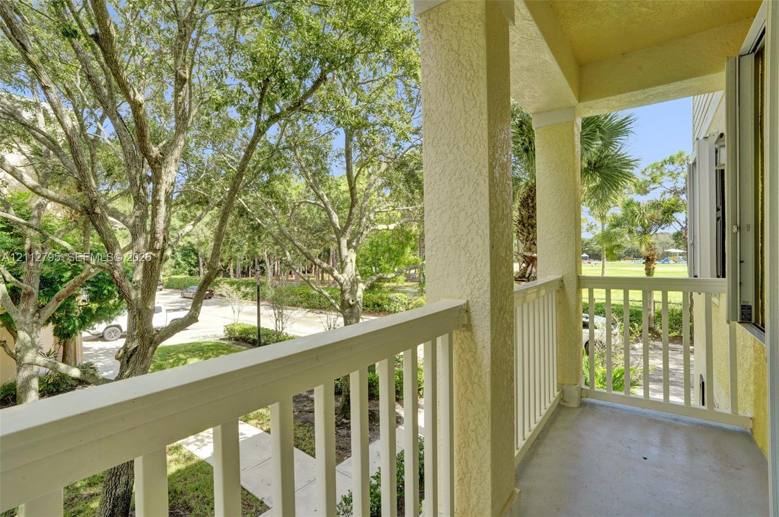 Covered balcony featuring white vertical railings, stucco columns, and concrete flooring