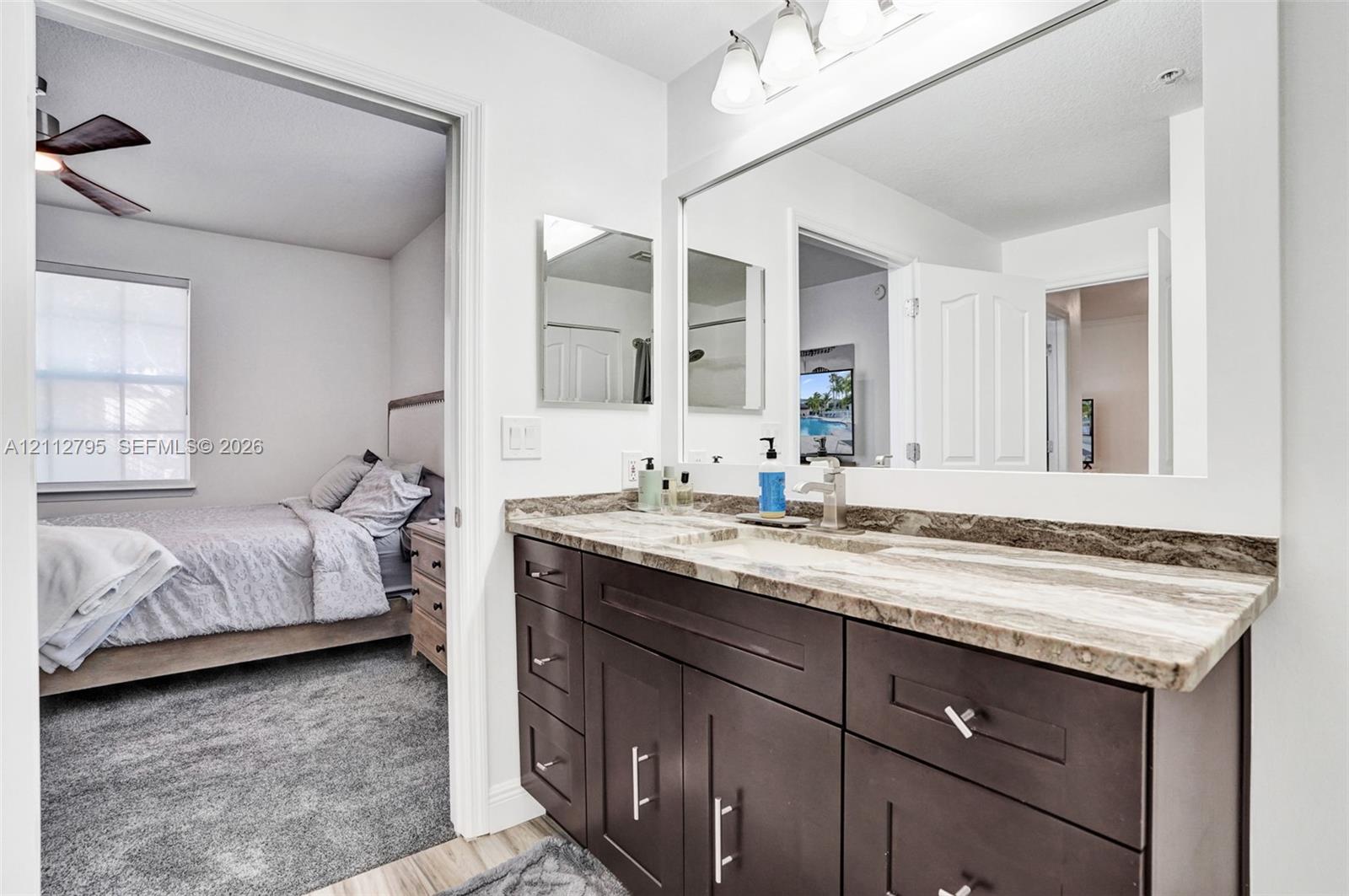 Bathroom vanity featuring dark-toned cabinetry, a stone-patterned countertop, an integrated sink with a metal faucet, a large wall-mounted mirror, and triple-bulb vanity lighting