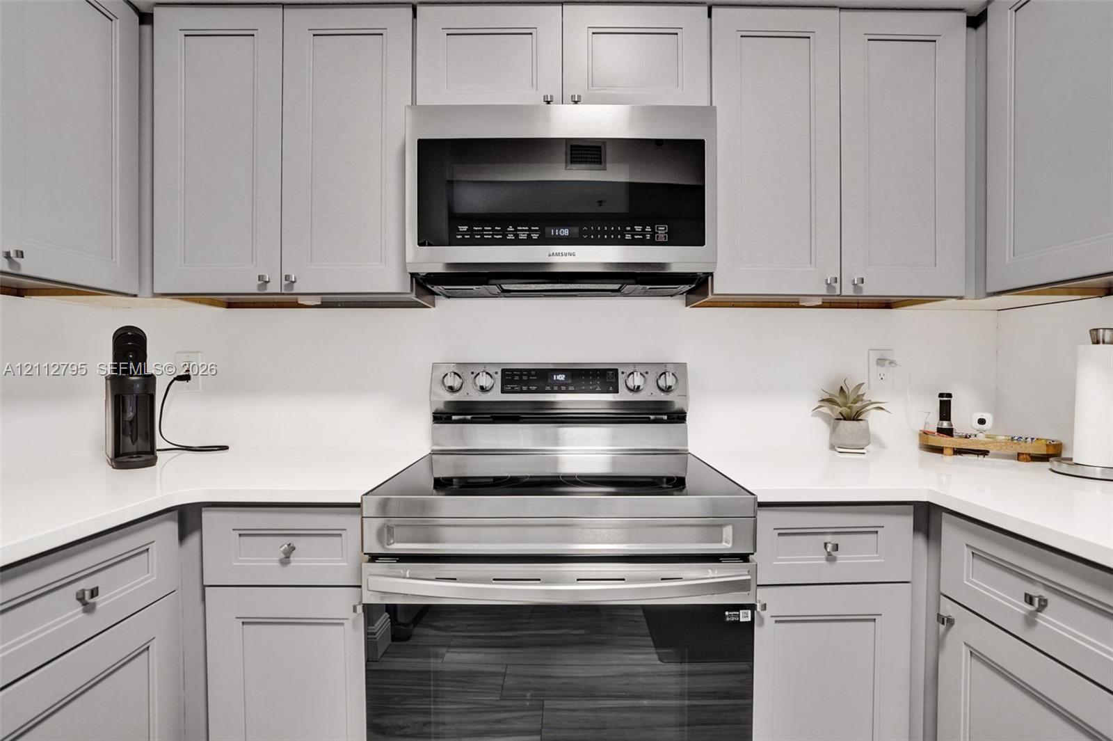Kitchen featuring grey shaker-style cabinetry, solid-surface countertops, and stainless steel appliances, including an over-the-range microwave and a smooth-top range