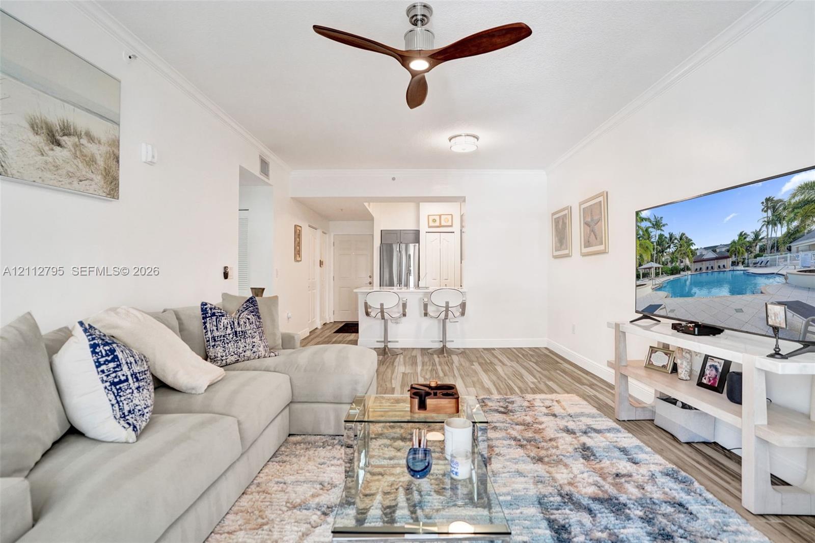 Open-concept room featuring wood-finish flooring, a contemporary three-blade ceiling fan, and crown molding