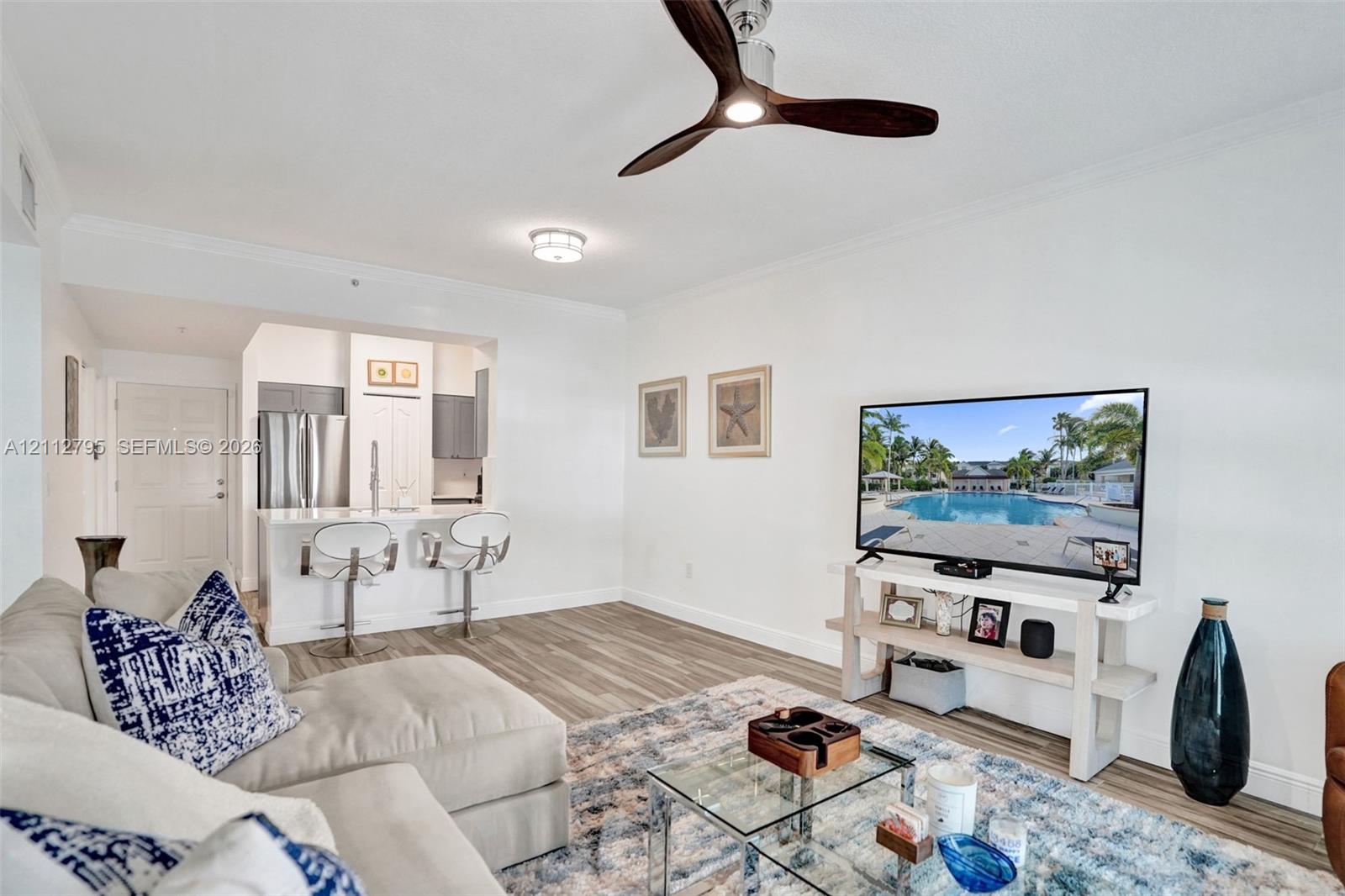 Open-concept living space featuring wood-finish flooring, a modern three-blade ceiling fan, and a kitchen pass-through with a stone-surface breakfast bar