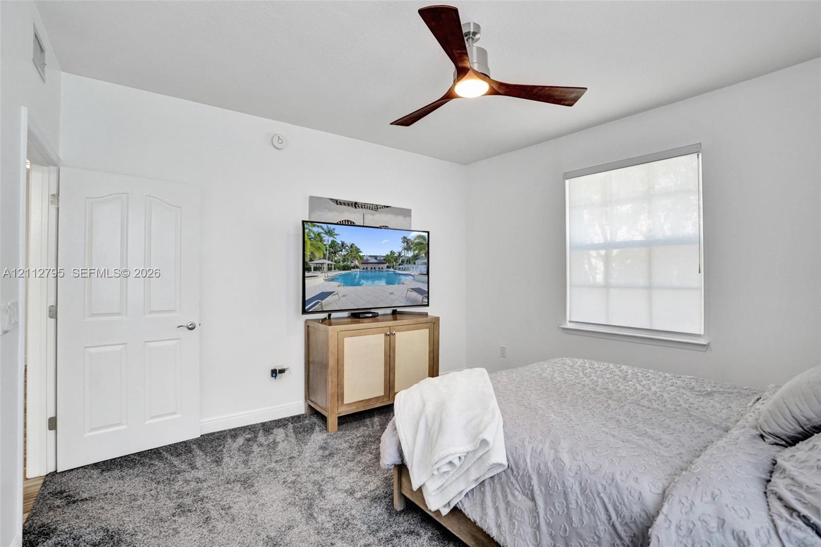 Neutral interior featuring wall-to-wall carpeting, a three-blade ceiling fan with integrated lighting, and a multi-pane window with a roller shade