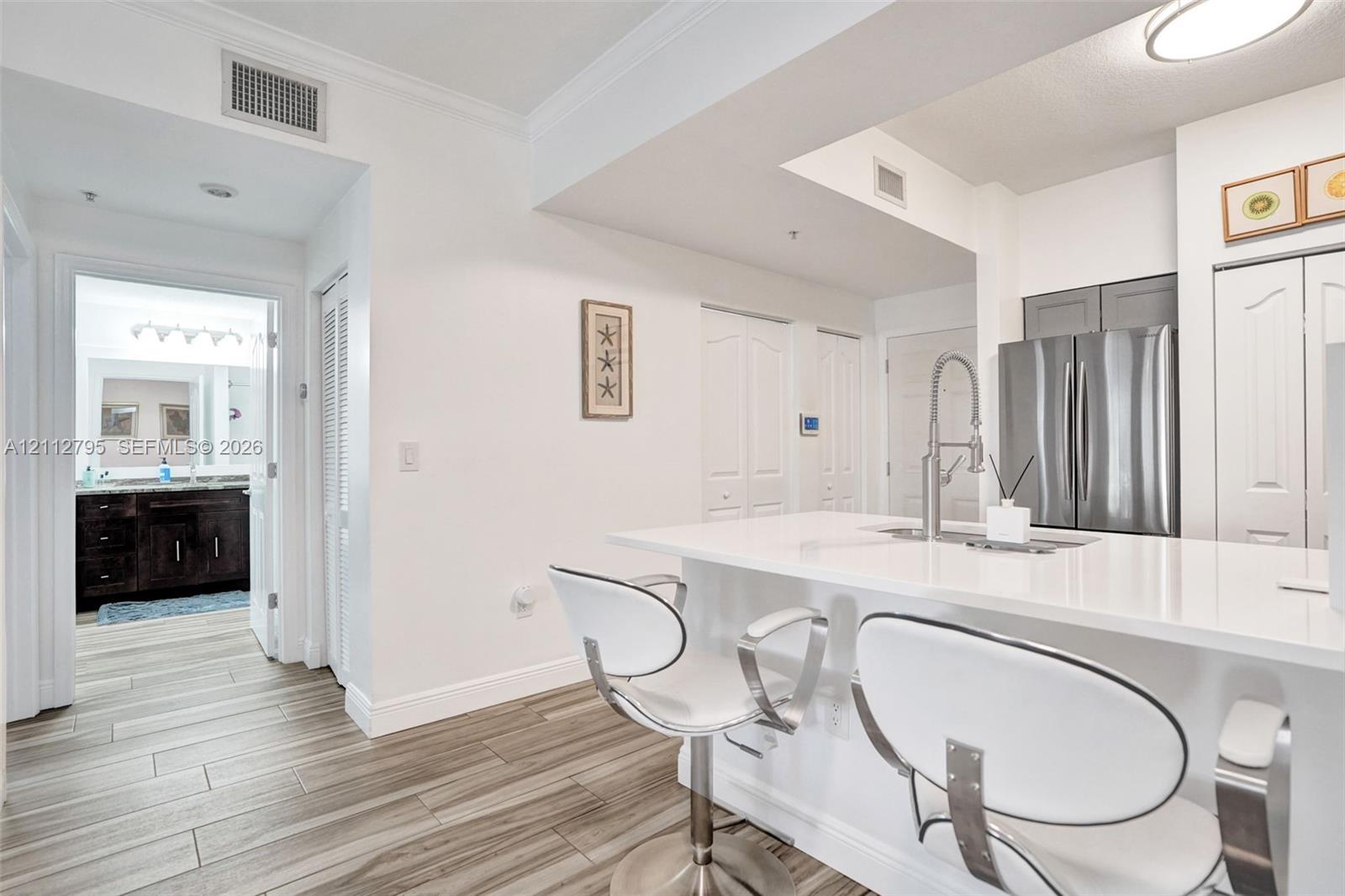 Kitchen featuring a breakfast bar with a solid surface countertop, stainless steel refrigerator, pull-down chrome faucet, and wood-finish flooring