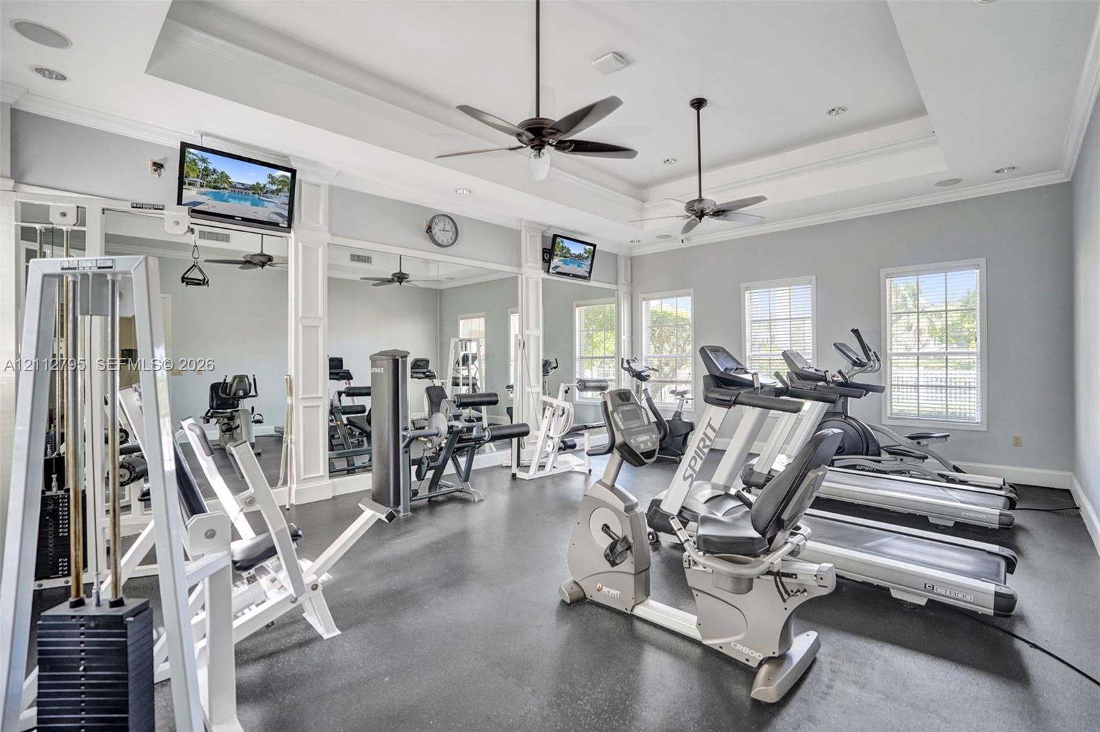 Fitness room featuring tray ceilings, full-wall mirrors, multi-blade ceiling fans, and rubber flooring