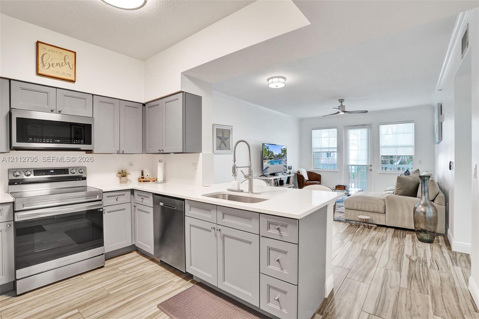 Kitchen featuring grey shaker cabinetry, white countertops, stainless steel appliances, a stainless steel undermount sink with a pull-down faucet, and wood-finish flooring
