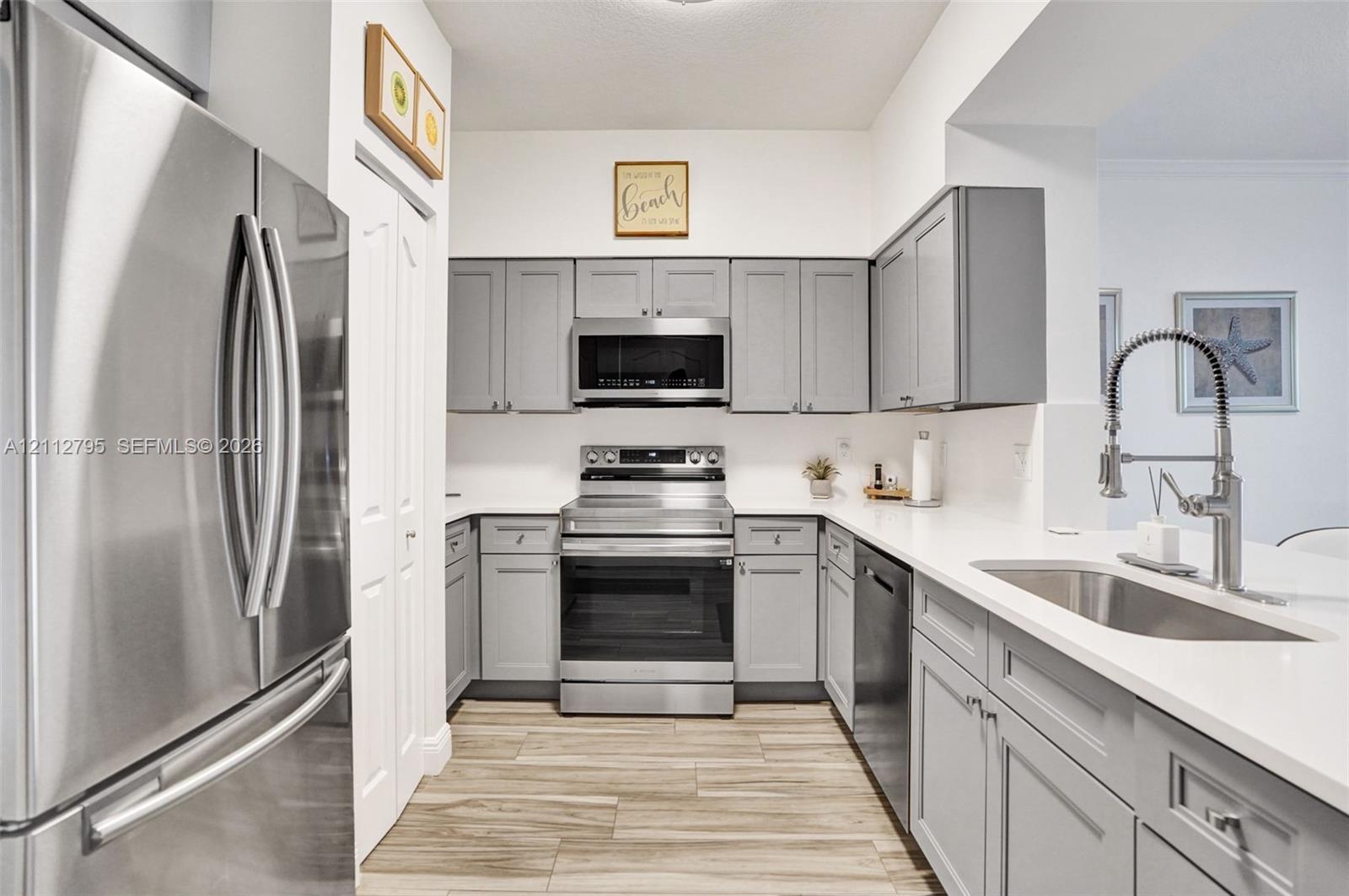 Kitchen featuring grey shaker-style cabinetry, stainless steel appliances, solid surface countertops, wood-finish tile flooring, and a gooseneck faucet