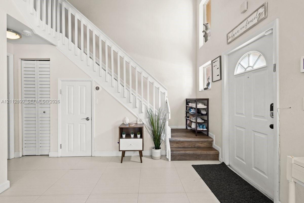 Entryway featuring tile flooring, high ceilings, a staircase with white balusters, louvered closet doors, and wood-finish stair treads