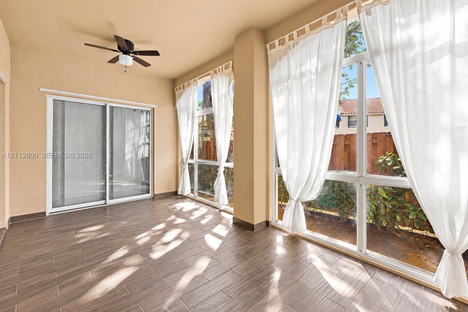 Covered patio featuring wood-finish tile flooring, a ceiling fan, and expansive floor-to-ceiling windows
