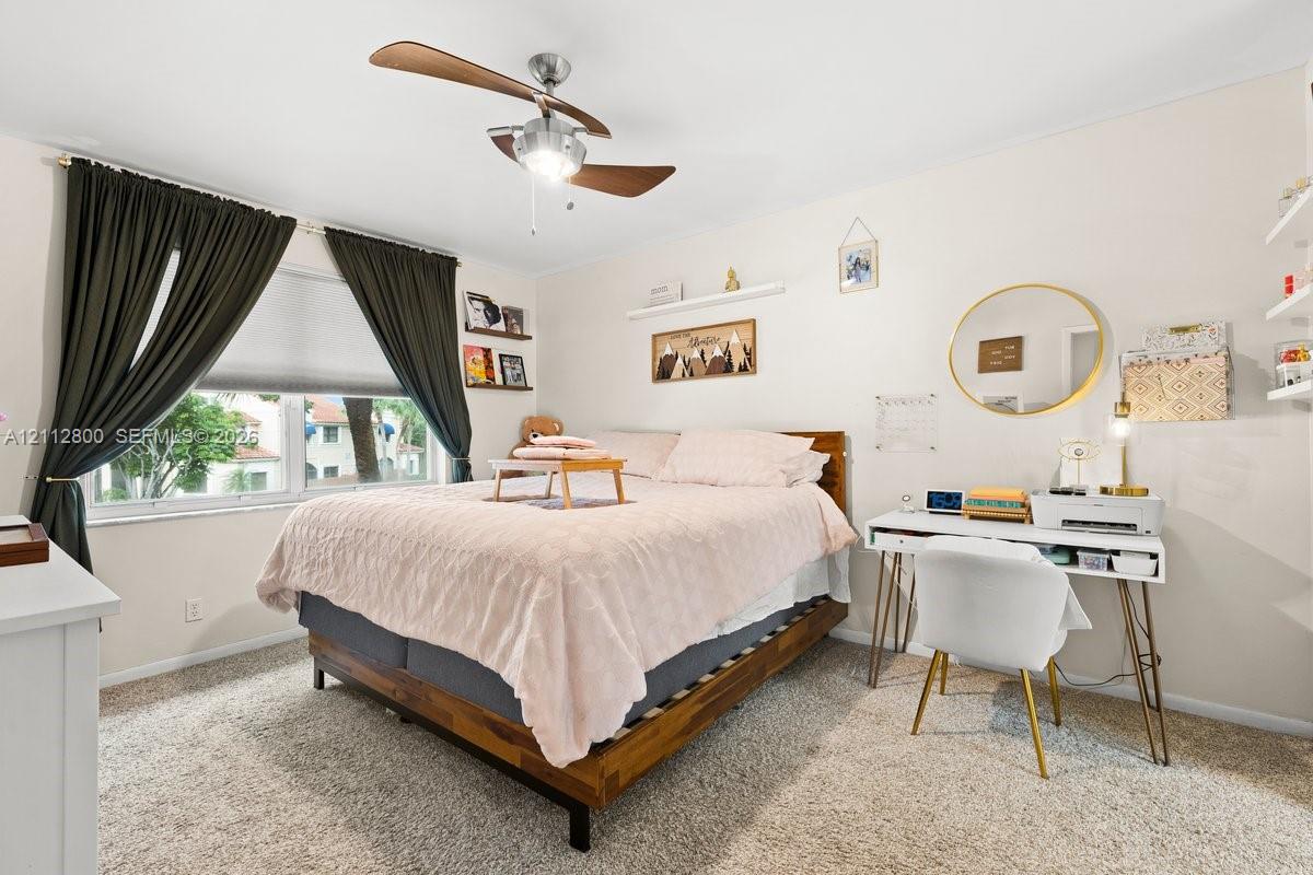 Bedroom featuring wall-to-wall carpeting, a multi-blade ceiling fan with integrated light fixture, two built-in wall shelves, and a double-pane window
