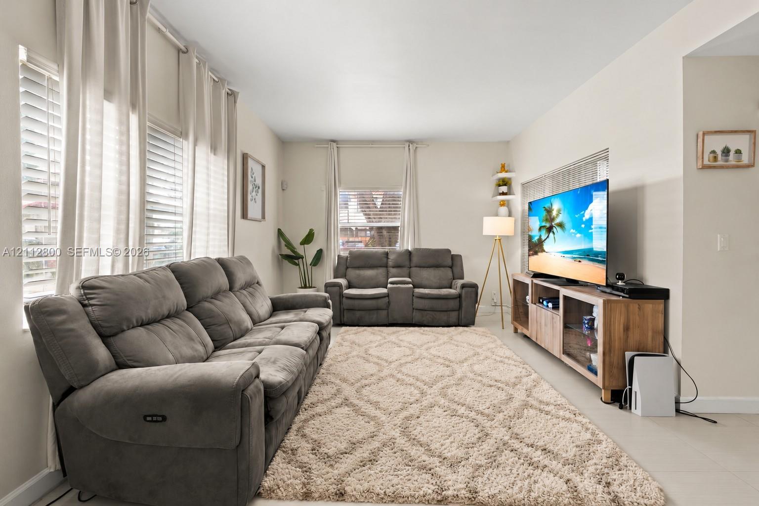Neutral-toned living space featuring large windows with window treatments, recessed lighting, and tile flooring