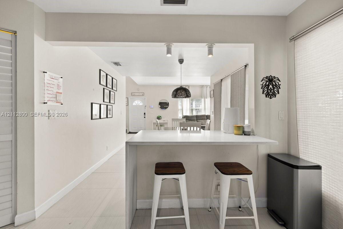 Breakfast bar with a waterfall-edge countertop, neutral wall color palette, large-format tile flooring, and metallic pendant lighting