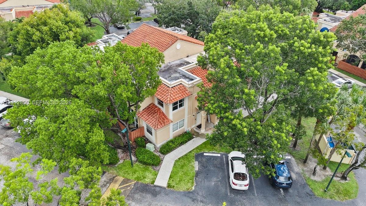 Aerial view of a multi-level structure featuring a terracotta tile roof, stucco exterior, paved walkway, and mature trees