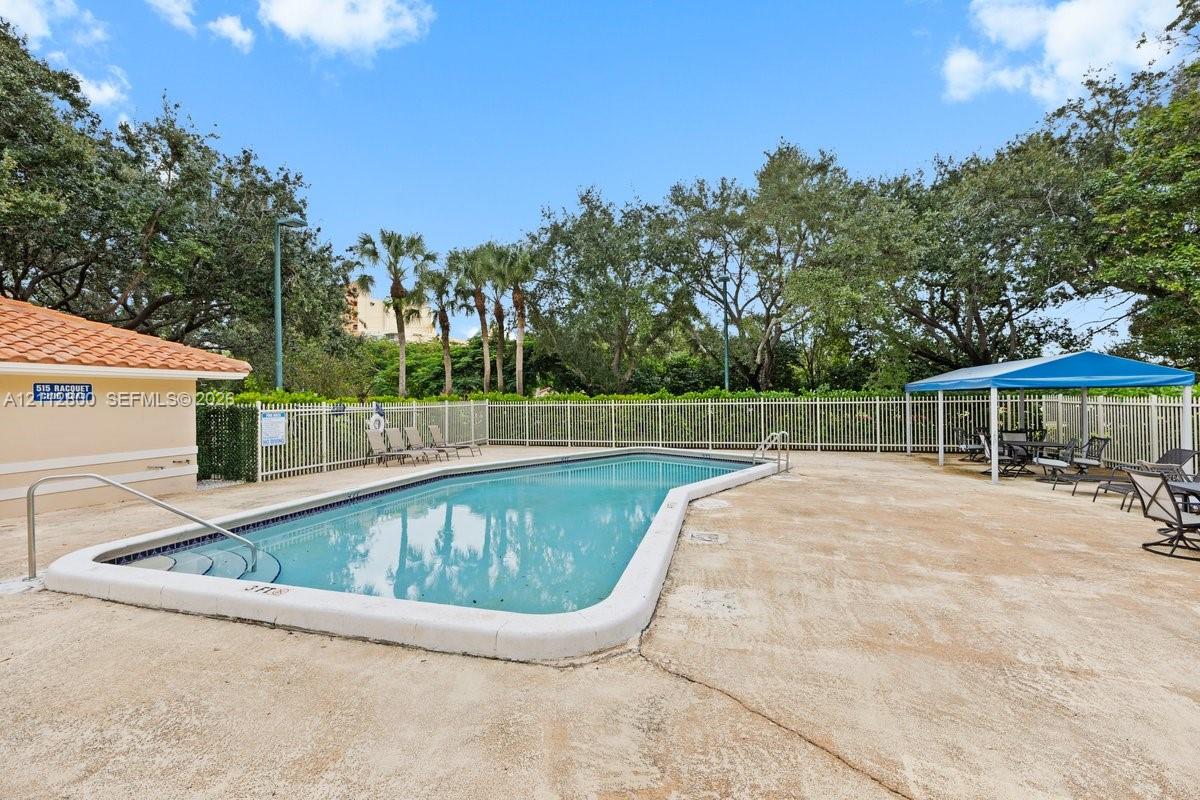 In-ground swimming pool featuring a concrete surround, metal perimeter fencing, and a shaded cabana area