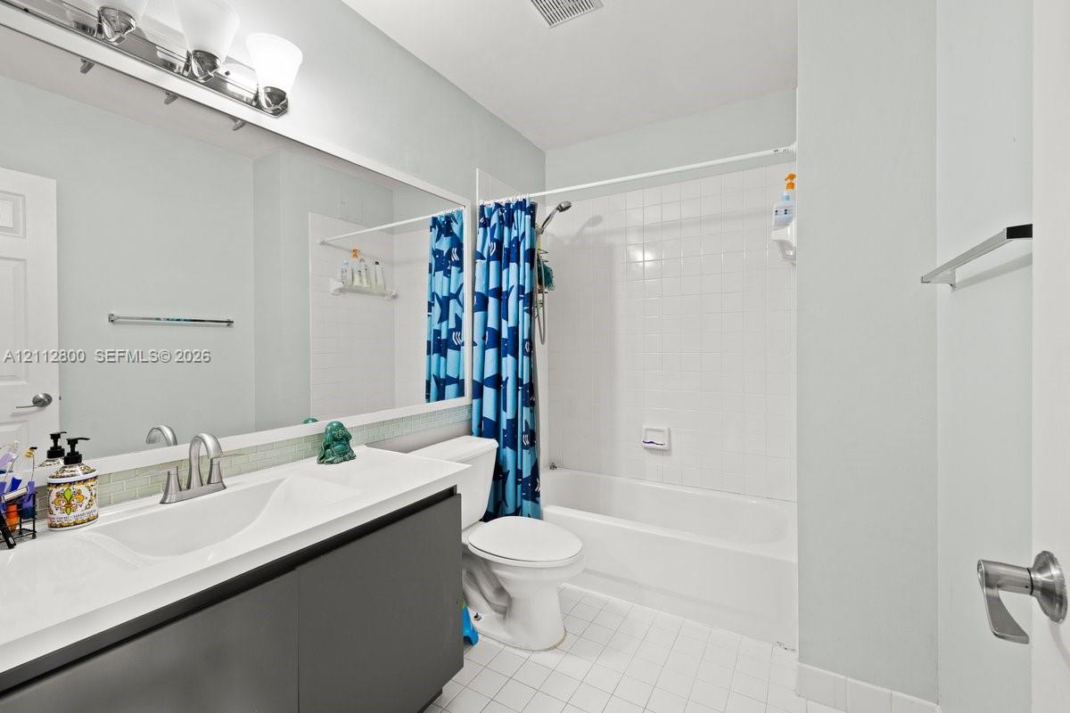 Full-width vanity with an integrated countertop, dark cabinetry, oversized wall mirror, three-light fixture, and a tub-shower combination with white tile surround