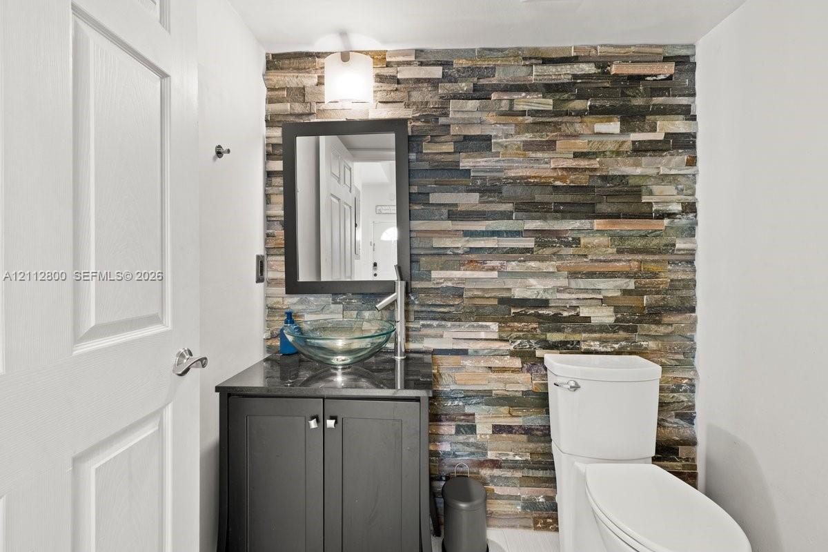 Stacked natural stone accent wall featuring a dark-finish vanity, glass vessel sink, sleek single-handle faucet, and framed wall-mounted mirror
