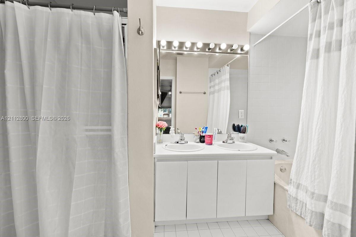 Bathroom featuring a dual-sink vanity with white cabinetry, a full-width vanity mirror, a multi-bulb light fixture, and a tiled shower-tub combination