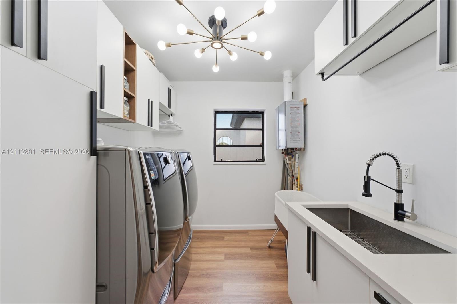 Laundry room featuring white cabinetry with matte black hardware, wood-finish flooring, quartz countertops, a stainless steel undermount sink with a gooseneck faucet, and a multi-arm sputnik-style light fixture