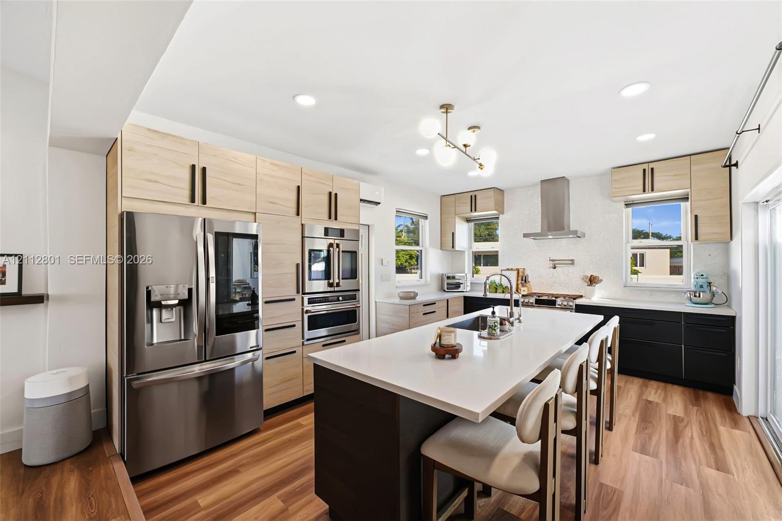 Kitchen featuring two-tone cabinetry, central island with light-toned countertop, stainless steel appliances, wood-finish flooring, and multi-globe chandelier lighting