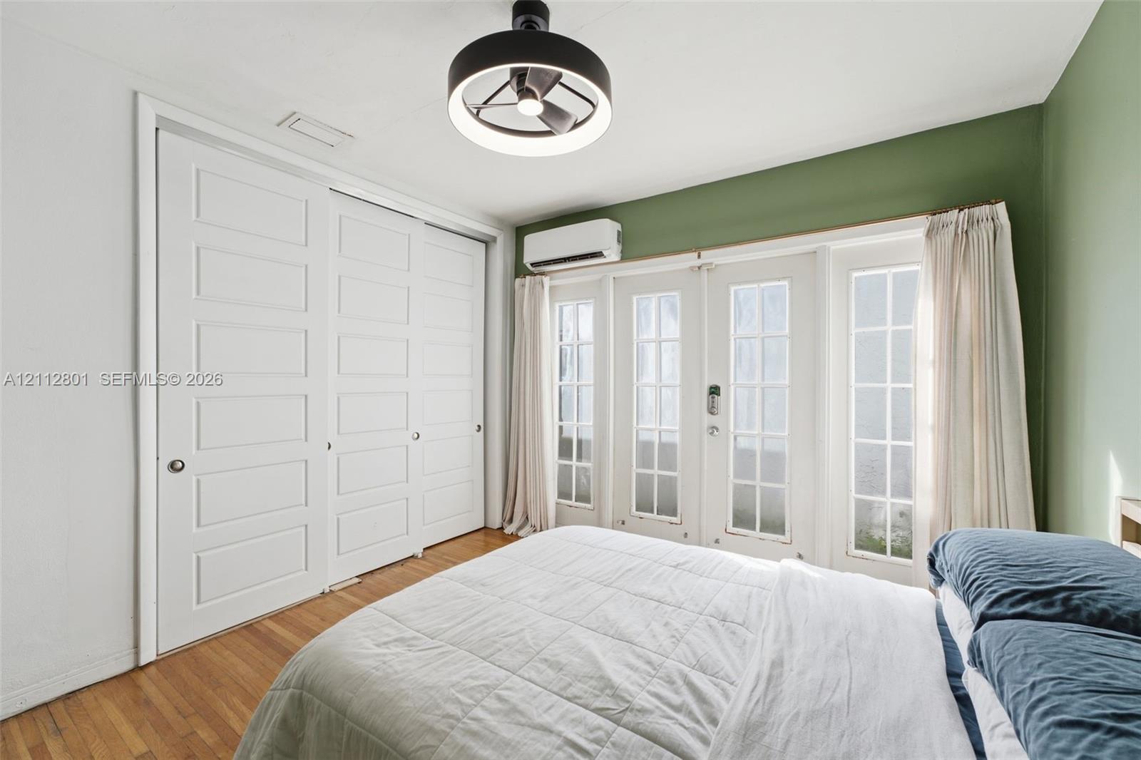 Room featuring wood-finish flooring, a wall-mounted ductless mini-split system, double glass-panel doors with grid detailing, and floor-to-ceiling built-in closet cabinetry