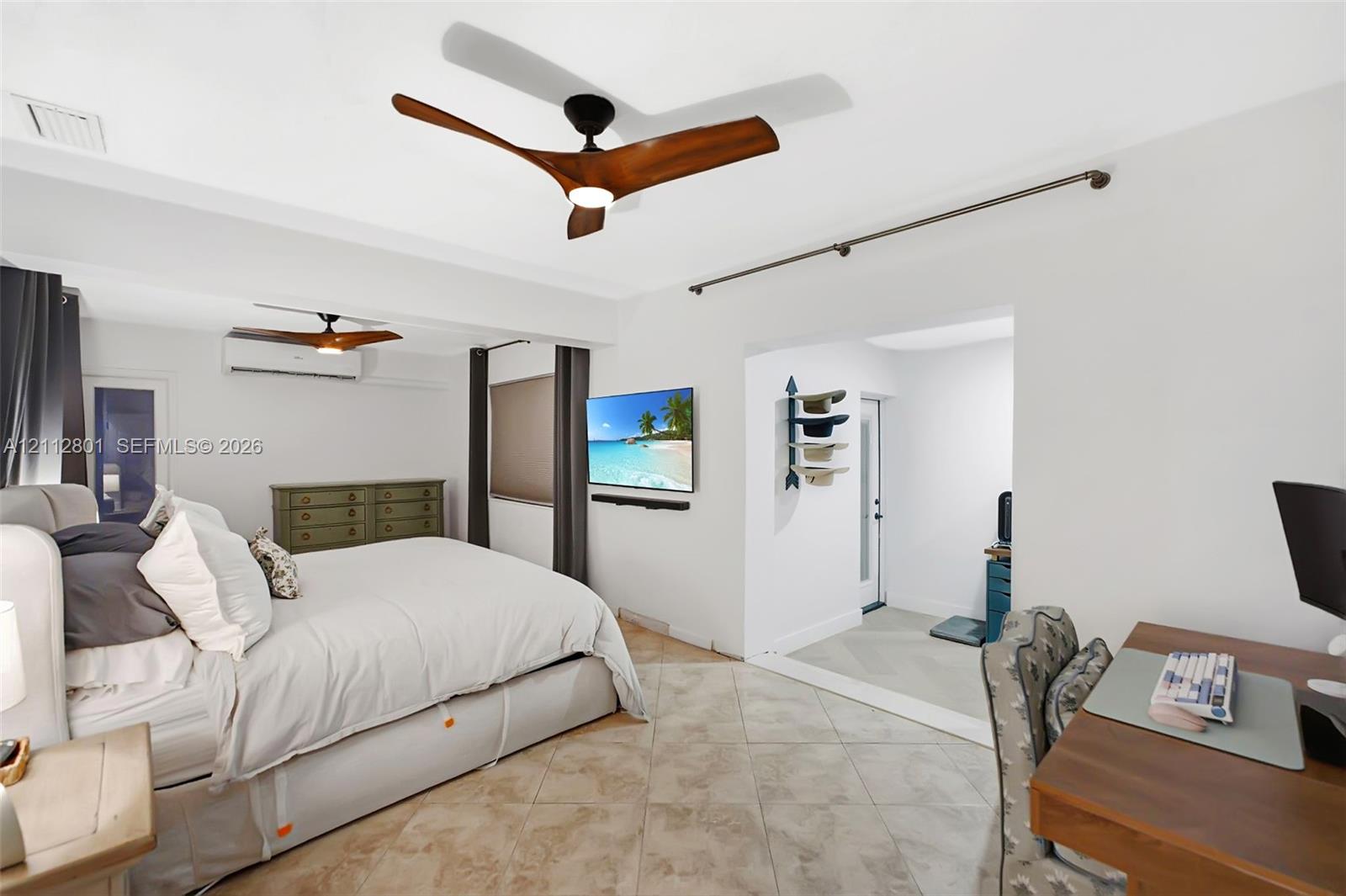 Spacious room featuring neutral stone-finish tile flooring, dual modern three-blade ceiling fans, and a wall-mounted ductless climate control unit