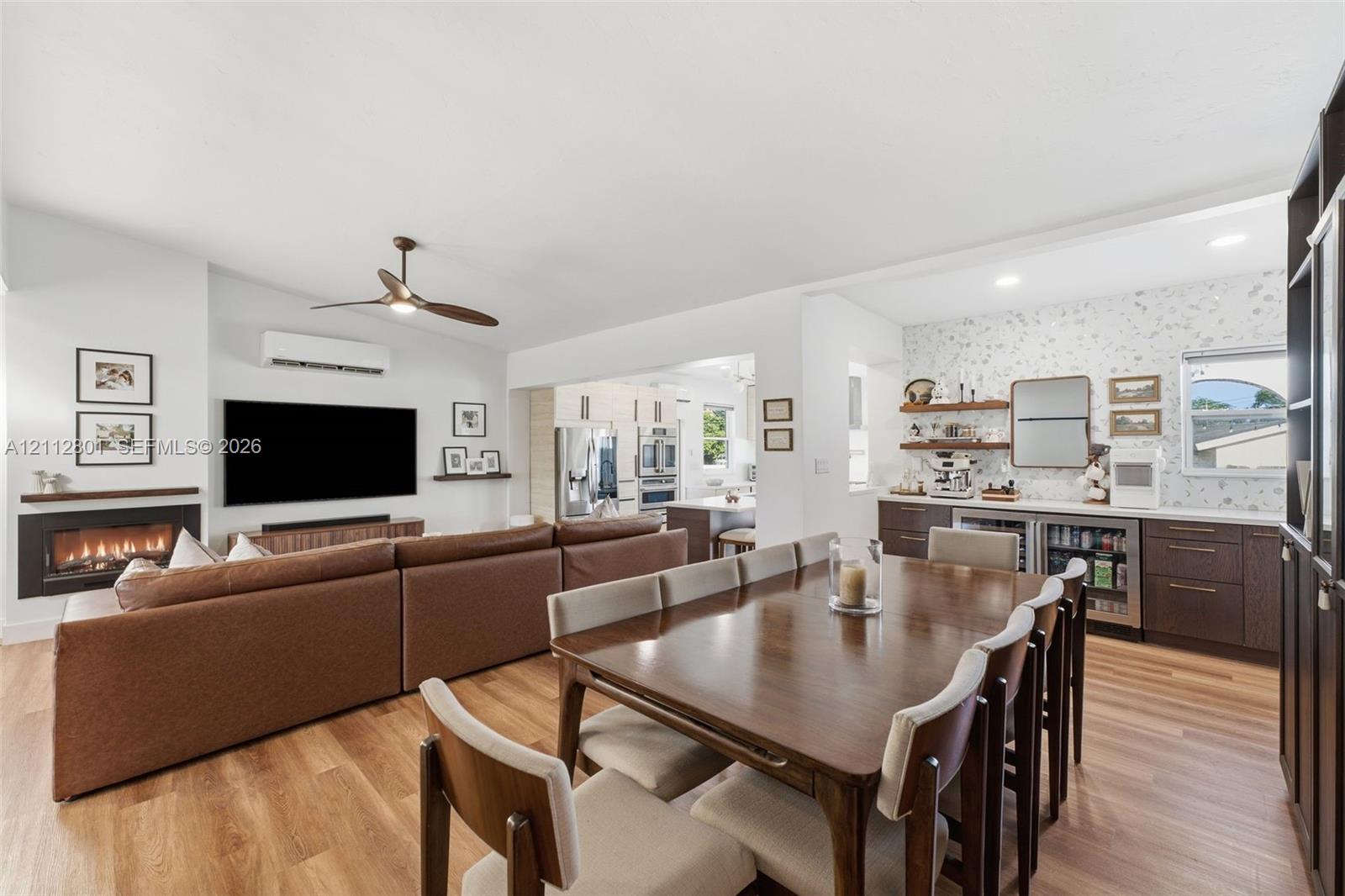 Open-concept living space featuring wood-finish flooring, a wall-mounted linear fireplace with a floating mantel, a ceiling fan, recessed lighting, and a built-in wet bar with dark cabinetry