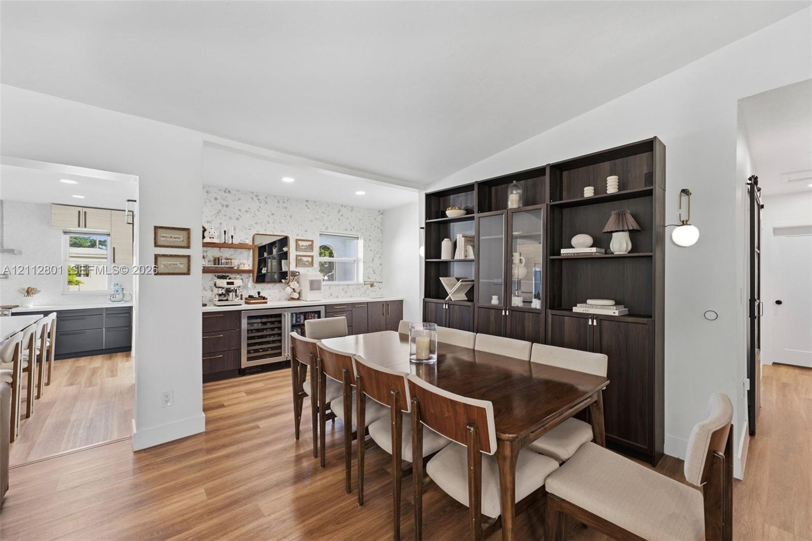 Wood-finish flooring, floor-to-ceiling dark wood built-in cabinetry, custom wet bar with under-counter refrigeration, recessed lighting, and modern wall-mounted light fixture