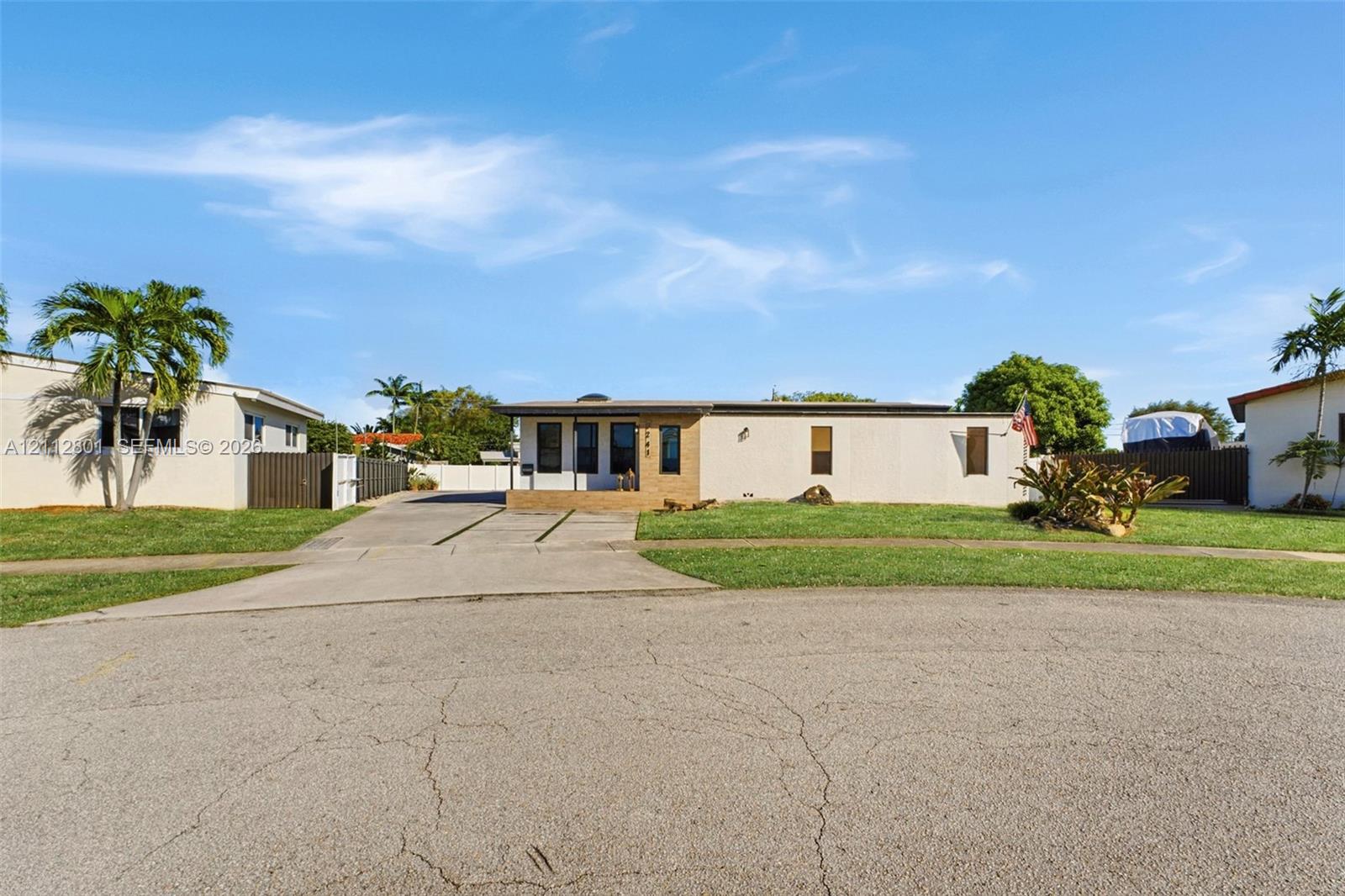 Single-story exterior featuring a light-toned stucco facade, concrete driveway, masonry retaining wall, and landscaping
