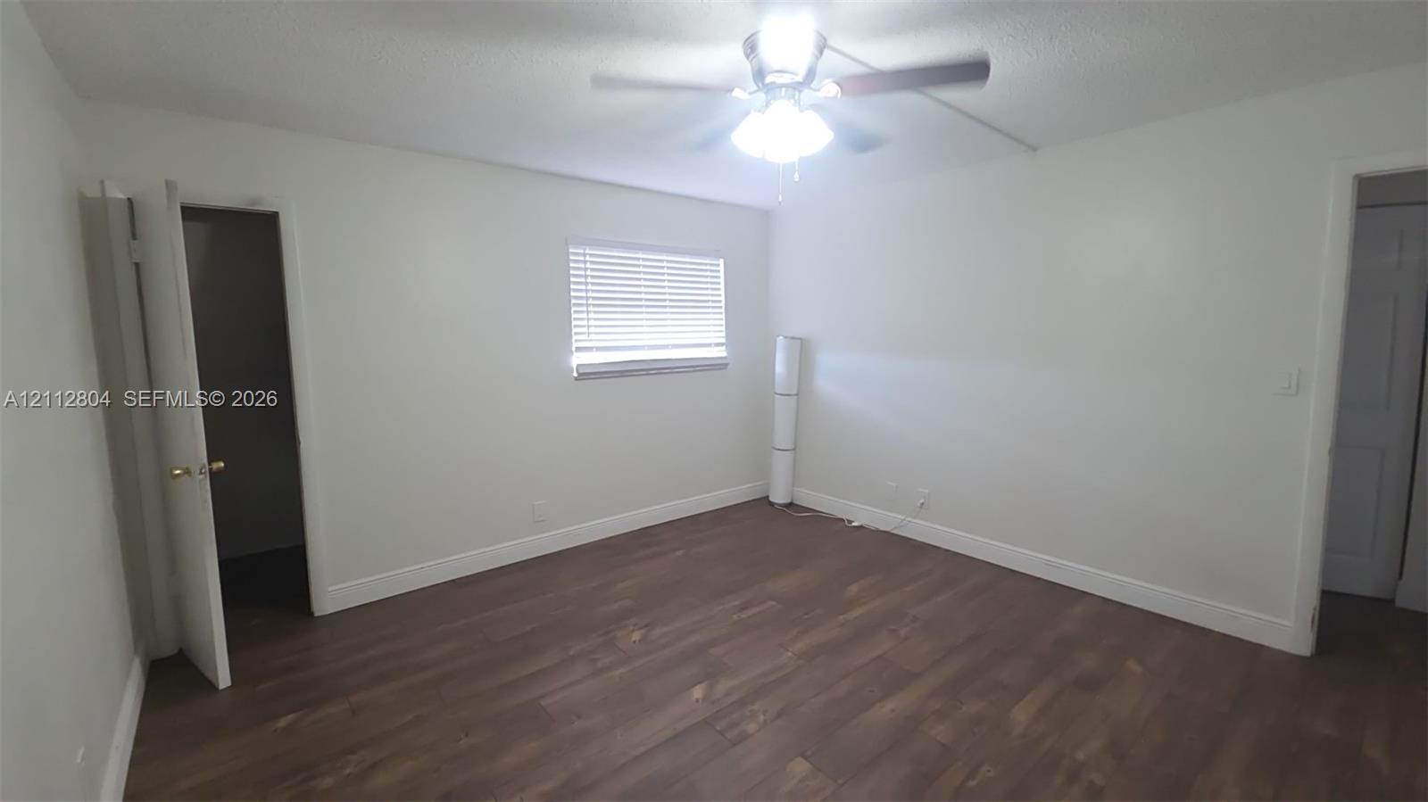 Room featuring dark wood-finish flooring, a ceiling fan with integrated lighting, and a window with horizontal blinds