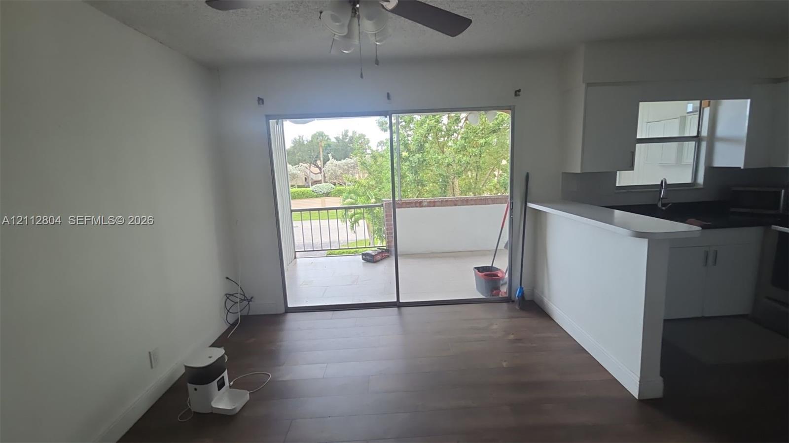 Sliding glass door, wood-finish flooring, ceiling fan, pass-through breakfast bar, and balcony with metal railing