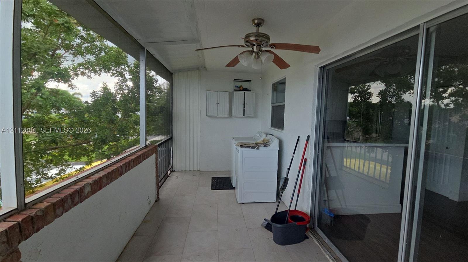 Enclosed patio featuring brick masonry detailing, tile flooring, a ceiling fan, and sliding glass entry doors