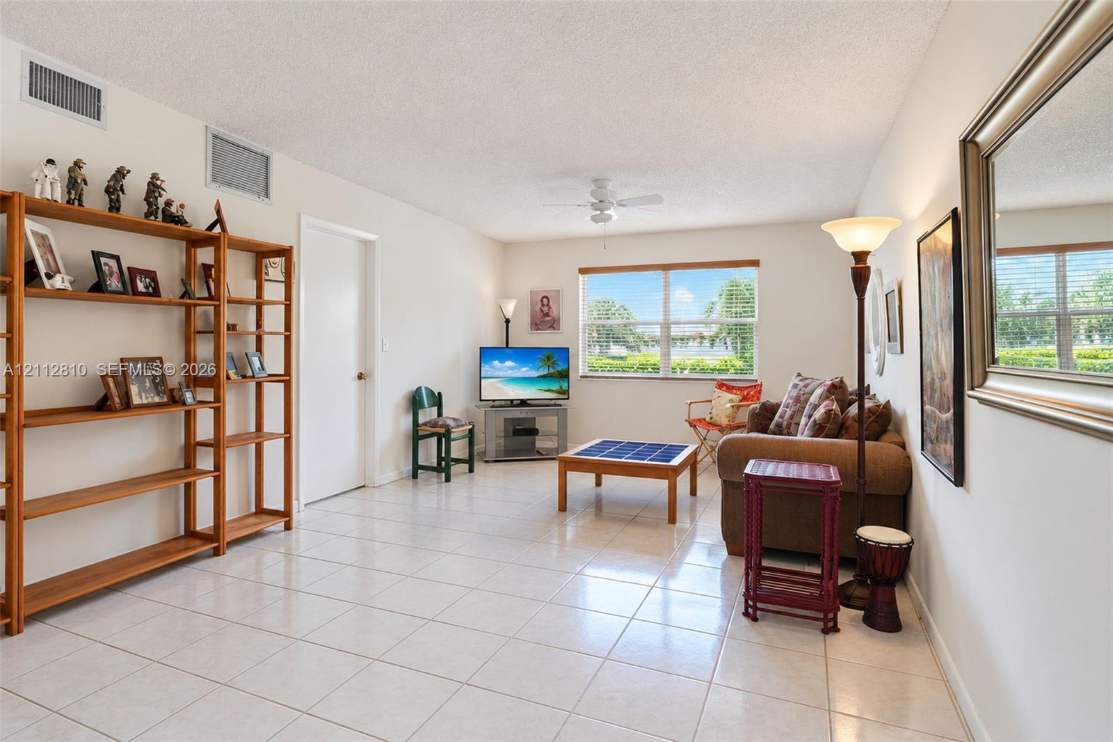 Living area featuring neutral tile flooring, a ceiling fan with integrated lighting, and a window with exterior scenery Living area featuring neutral tile flooring, a ceiling fan with integrated lighting, and a window with exterior scenery