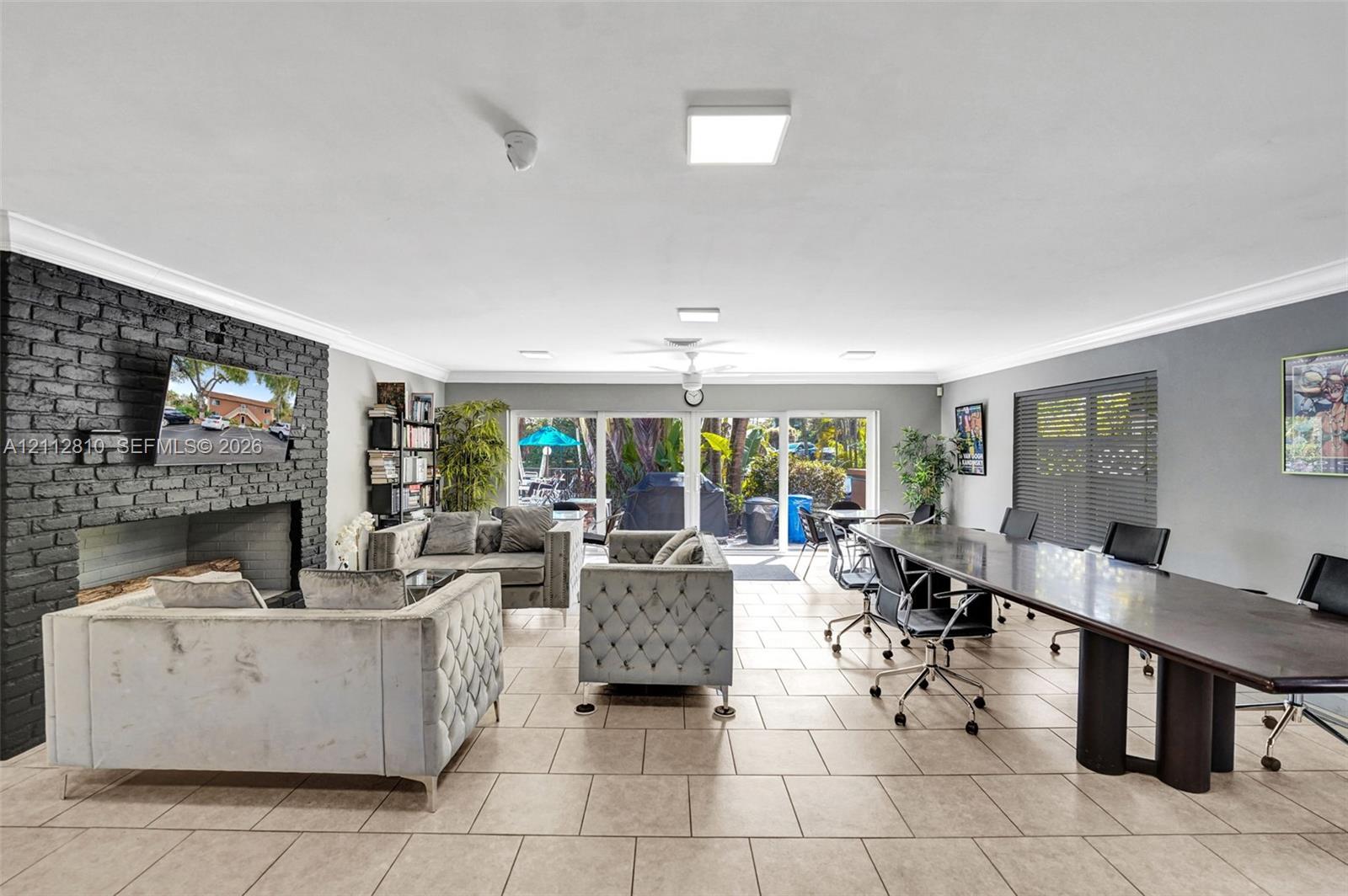 Interior space featuring tile flooring, a floor-to-ceiling painted brick fireplace surround, crown molding, and glass sliding doors