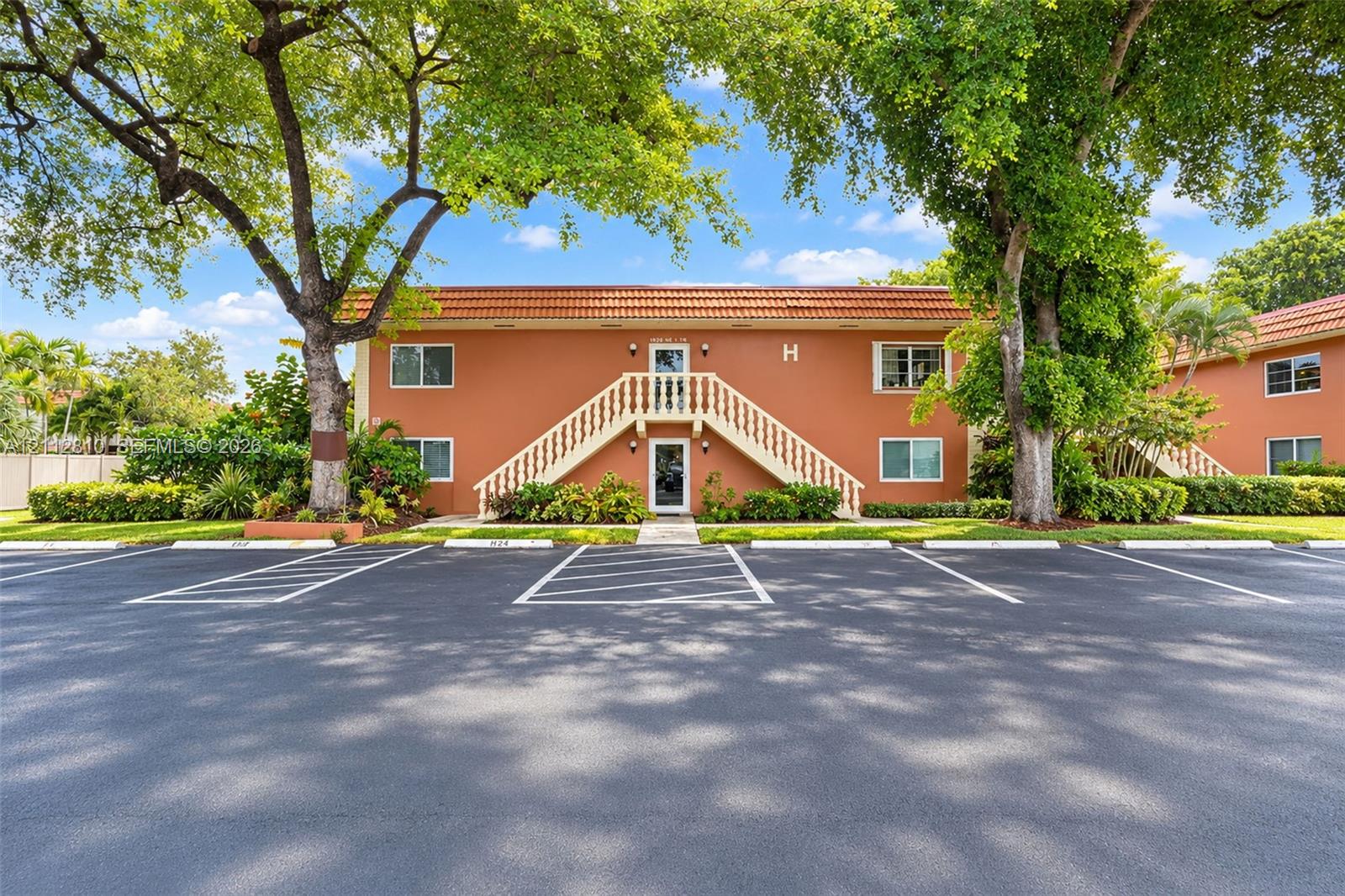 Two-story exterior featuring a clay tile roof, stucco facade, external staircase with balustrade railings, and paved surface parking Two-story exterior featuring a clay tile roof, stucco facade, external staircase with balustrade railings, and paved surface parking