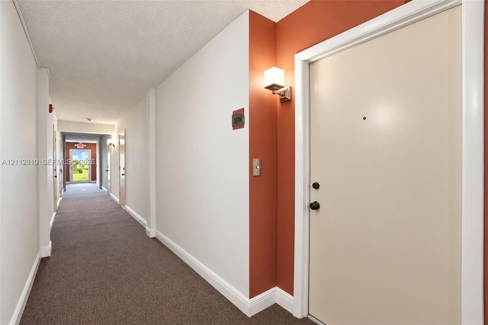 Interior hallway featuring carpeting, accent wall paint, and wall-mounted lighting fixtures Interior hallway featuring carpeting, accent wall paint, and wall-mounted lighting fixtures